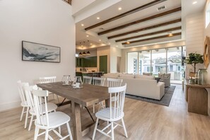 A spacious living area with a wooden dining table and white chairs, a white sofa, and a kitchen in the background. - Stunning Vanderbilt Beach House With Heated Pool (Naples)