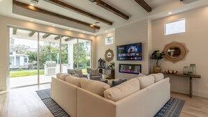 A modern living room with a large sectional sofa, a flat-screen TV, and a fireplace. - Stunning Vanderbilt Beach House With Heated Pool (Naples)