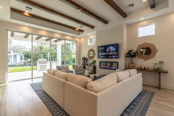 A modern living room with a large sectional sofa, a flat-screen TV, and a fireplace. - Stunning Vanderbilt Beach House With Heated Pool (Naples)