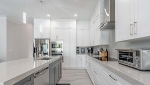 A modern kitchen with white cabinetry, stainless steel appliances, and a marble countertop. - Sparkling new Vanderbilt Beach Luxury Escape (Naples)