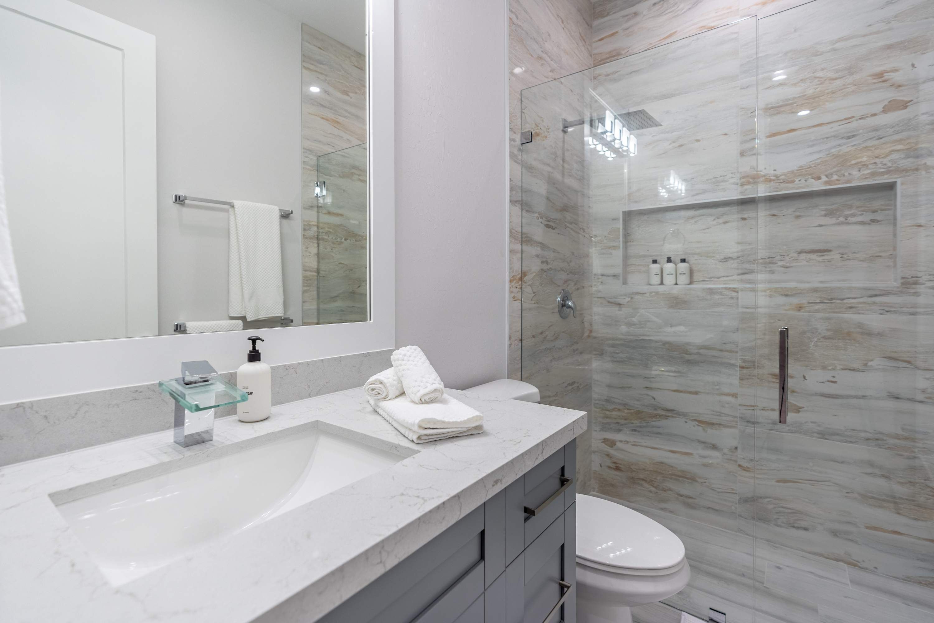 A modern bathroom with a marble sink, a glass shower enclosure, and a toilet.