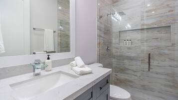 A modern bathroom with a marble sink, a glass shower enclosure, and a toilet.