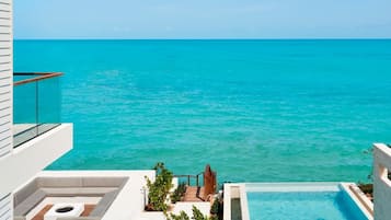 A modern pool area with a clear view of the ocean, lounge chairs, and a person swimming.