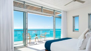 Habitación de hotel moderna con una cama grande, ventilador de techo y balcón con vista al océano.