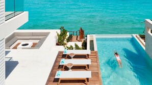 Un área de piscina moderna con vista despejada al océano, sillas de descanso y una persona nadando.