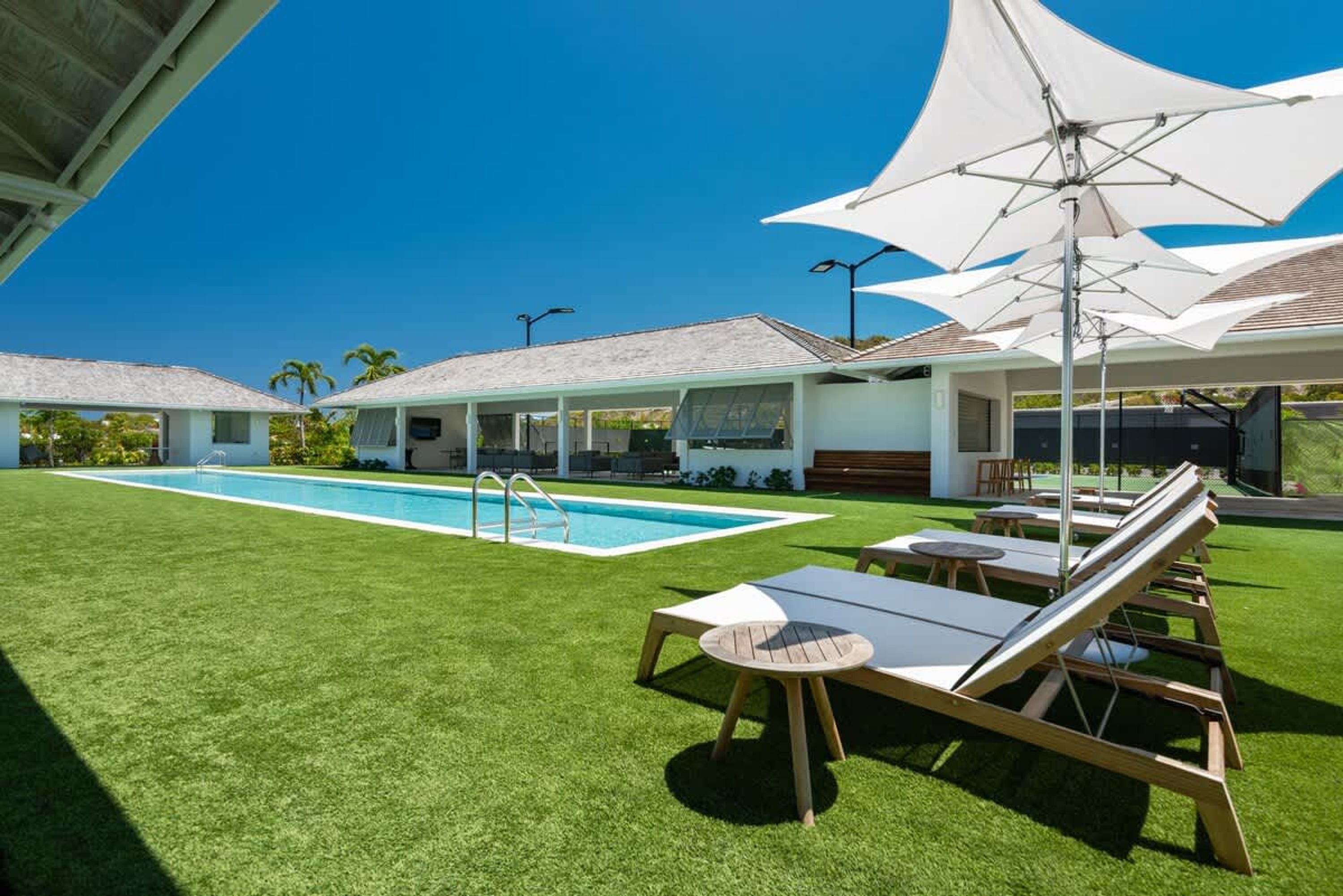 A pool area with lounge chairs and umbrellas, surrounded by a well-maintained lawn and a building with a tiled roof.