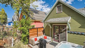 Une terrasse avec un jacuzzi, une clôture en bois et un bâtiment bleu en arrière-plan.