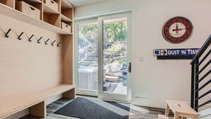Une pièce comprenant un banc, un porte-manteau fixé au mur, une porte donnant sur l’extérieur, une horloge et un panneau affiché sur le mur.
