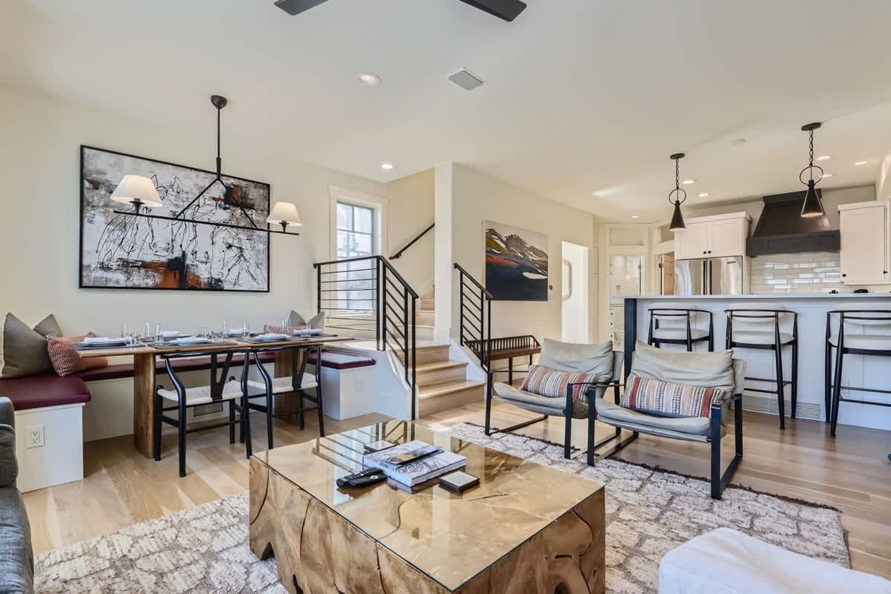A spacious living area with a dining table, sofa, and coffee table. There is a staircase leading to another level, and a kitchen area with modern appliances.