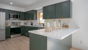 A modern kitchen with dark green cabinets, a central island, and stainless steel appliances. - Billingswood by Boutiq (Athens)