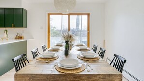 A dining room with a long wooden table set for eight, surrounded by black chairs, a hanging light fixture, and a view through a large window. - Billingswood by Boutiq (Athens)