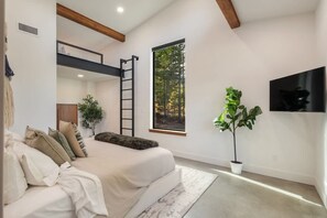 A modern bedroom with a bunk bed, a large window with a forest view, a potted plant, and a mounted TV. - Architecturally Stunning Cle Elum Luxury Retreat (Cle Elum)