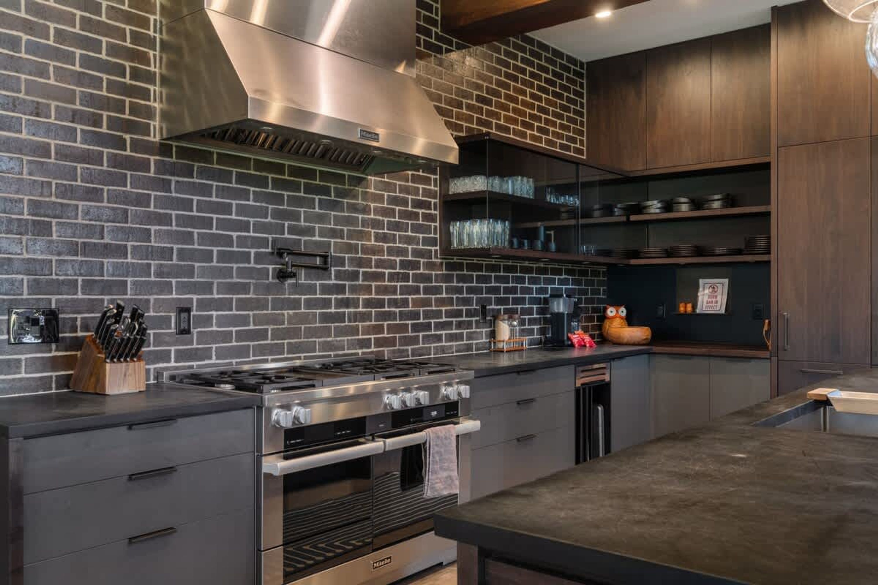 A modern kitchen with a brick backsplash, stainless steel appliances, and wooden cabinets.