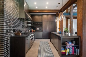 A modern kitchen with dark cabinetry, a brick accent wall, and a central island. - Architecturally Stunning Cle Elum Luxury Retreat (Cle Elum)