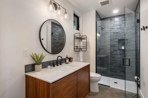 A modern bathroom with a round mirror, a wooden vanity, a glass shower enclosure, and a white toilet. - Architecturally Stunning Cle Elum Luxury Retreat (Cle Elum)