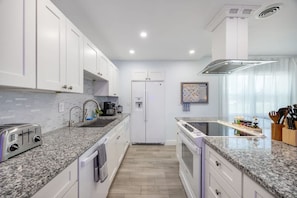 Una cocina moderna con armarios blancos, encimeras de granito, horno empotrado y campana extractora de acero inoxidable.