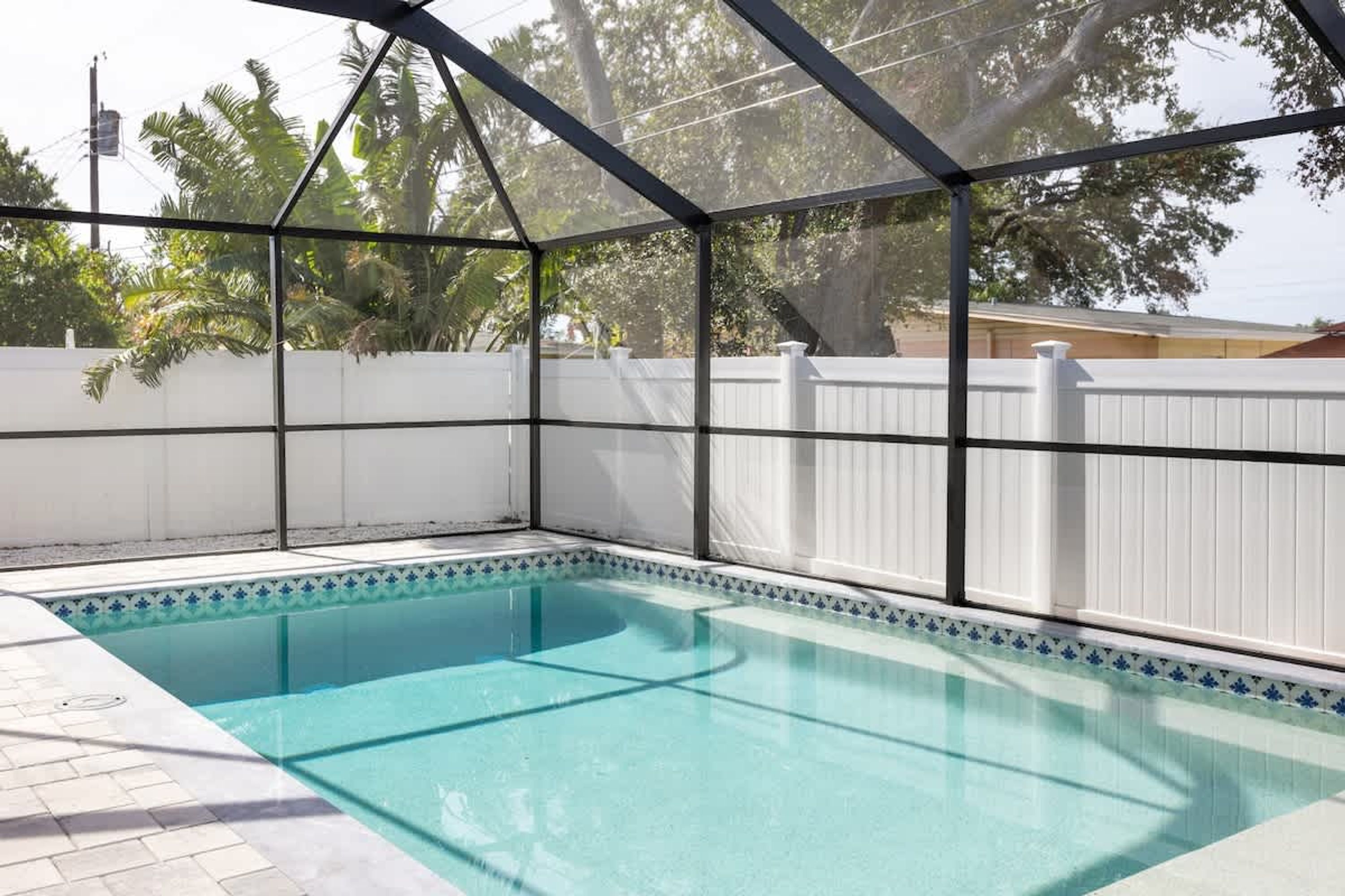 A swimming pool with a glass enclosure, surrounded by a white fence and a tiled deck.