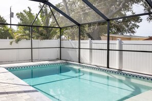 Una piscina con cerramiento de vidrio, rodeada por una valla blanca y un suelo de baldosas.
