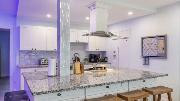 A modern kitchen with white cabinets, a granite countertop, and a central island with bar stools. - Fun Family-friendly Largo Home Heated Pool (Largo)