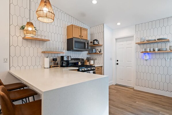 A modern kitchen with a central island, wooden cabinets, and a microwave. - J-tree Bungalow With Large Hot Tub Views Patio (Joshua Tree)