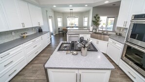 A modern kitchen with white cabinets, a granite countertop, stainless steel appliances, and a central island with a stove and sink. - Lavish Lake Havasu Villa Pool Fire Pit an Views (Lake Havasu City)