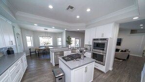 A spacious kitchen with white cabinetry, a central island, stainless steel appliances, and a dining area with a chandelier. - Lavish Lake Havasu Villa Pool Fire Pit an Views (Lake Havasu City)