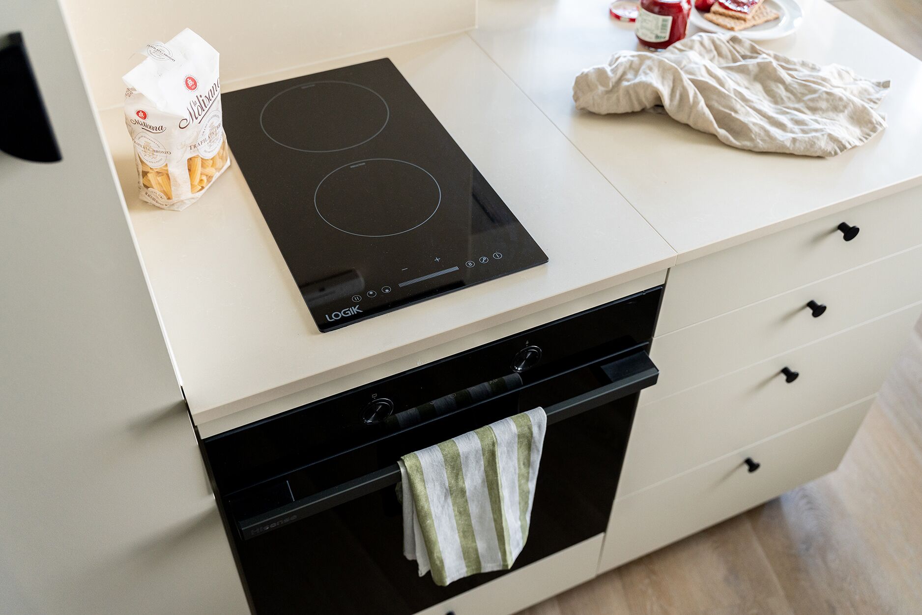 Een moderne keuken met een zwart inductiefornuis, een wit aanrechtblad en een zwarte oven.