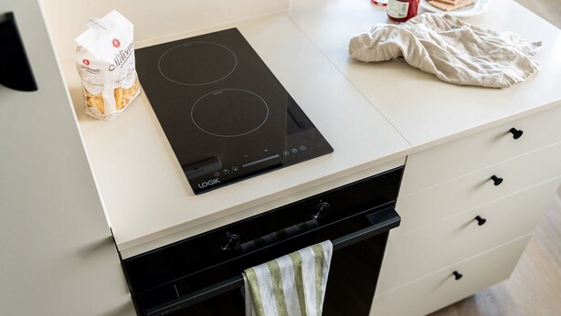 Une cuisine moderne dotée d’une plaque de cuisson à induction noire, d’un plan de travail blanc et d’un four noir.