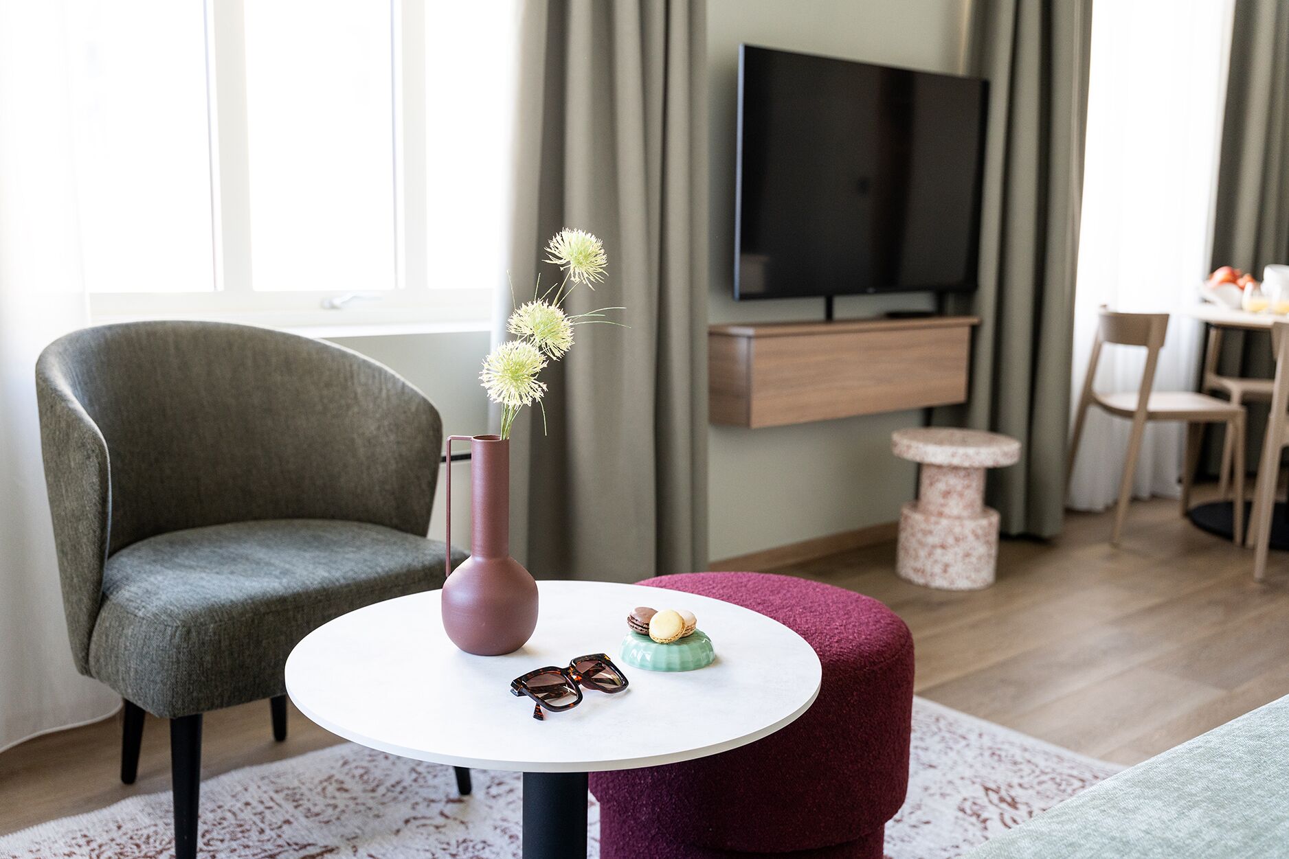 Una sala de estar moderna con un sillón gris, una mesa redonda con un florero y objetos decorativos, un televisor y un mueble de madera.