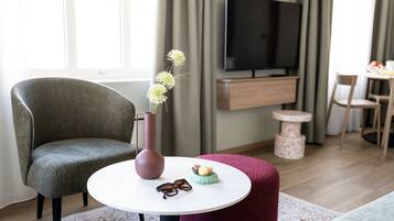 Una sala de estar moderna con un sillón gris, una mesa redonda con un florero y objetos decorativos, un televisor y un mueble de madera.