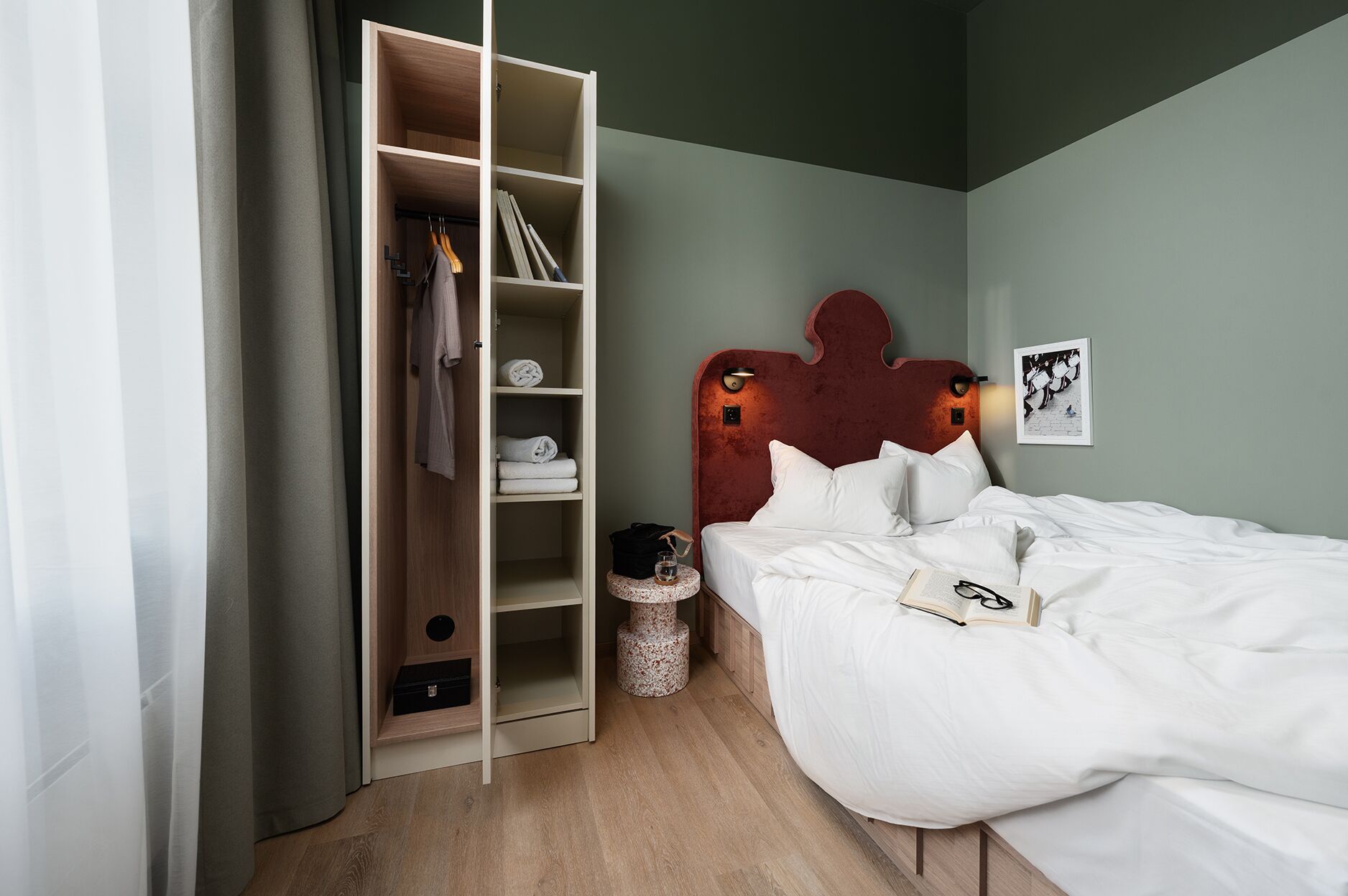 A bedroom with a bed, a wardrobe, and a small round table with a book and glasses.