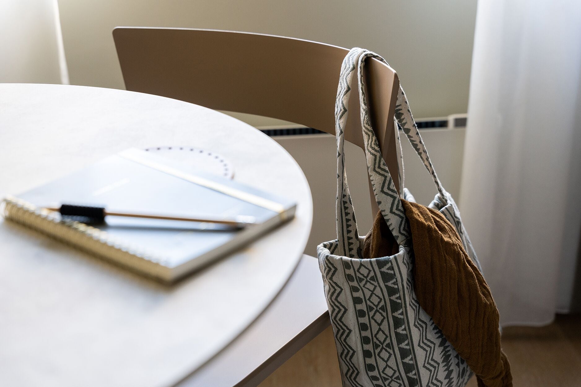 Una mesa redonda con un cuaderno, un bolígrafo y una bolsa estampada.