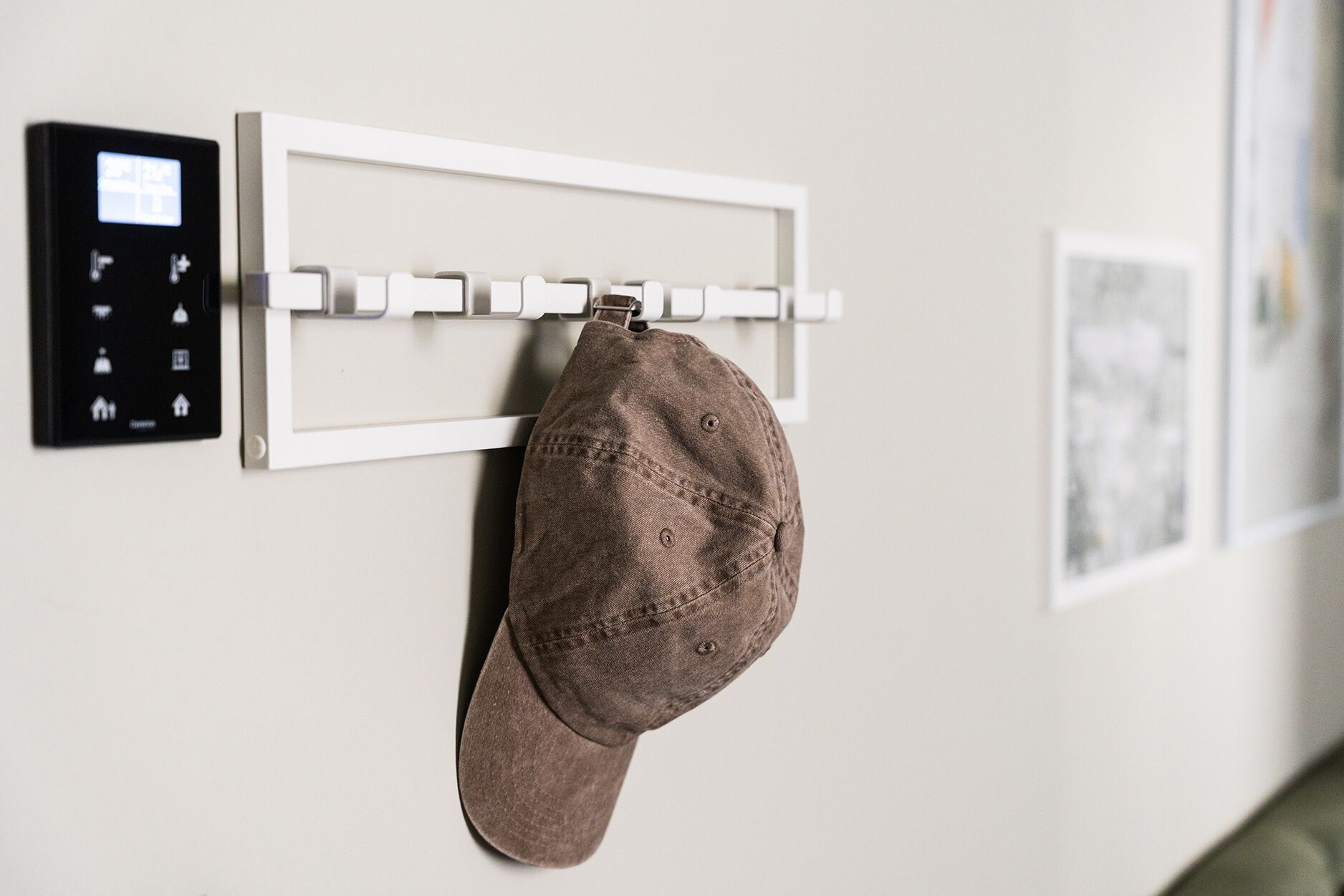 Un gancho para abrigos en la pared con un gorro colgado, un panel de control y un cuadro enmarcado.