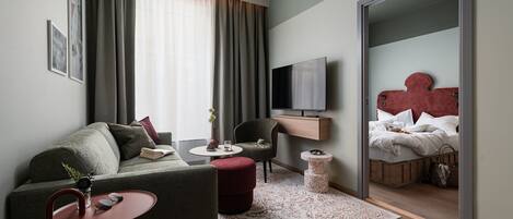 A modern hotel room with a sofa, armchair, TV, and a bed with a unique headboard.