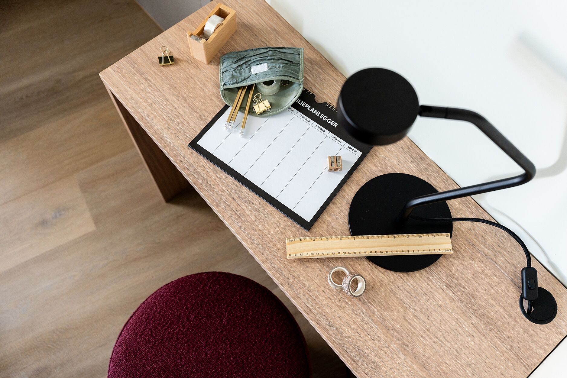 A wooden desk with a calendar, a tape dispenser, a ruler, and a pair of rings.