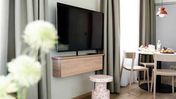 Un soggiorno moderno con una TV a schermo piatto montata a parete, un mobiletto in legno sottostante, una cuccia rotonda per animali domestici e un'area pranzo con sedie e un tavolo.