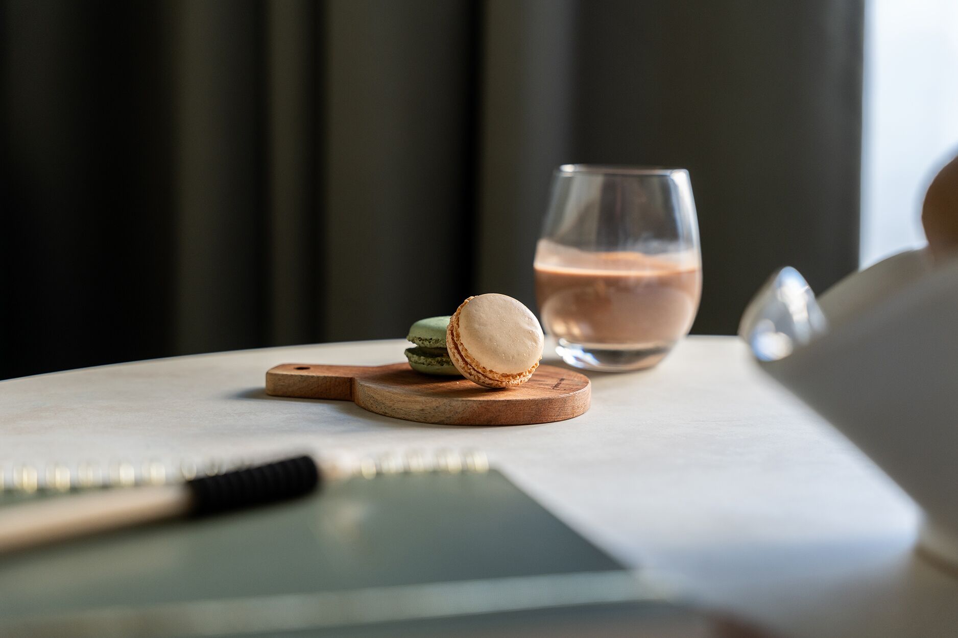 A table with a glass of iced coffee, two macarons, and a notebook.