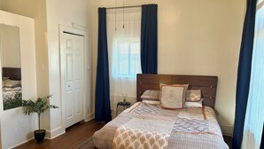 Une chambre à coucher avec un lit en bois, une plante en pot, un miroir et une fenêtre avec des rideaux.