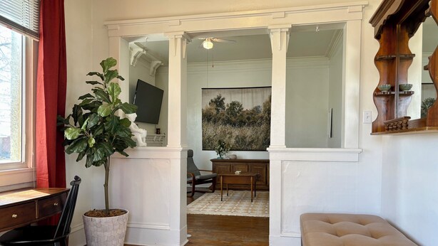 Une pièce avec un bureau en bois, une grande plante en pot, un canapé beige et un grand miroir.