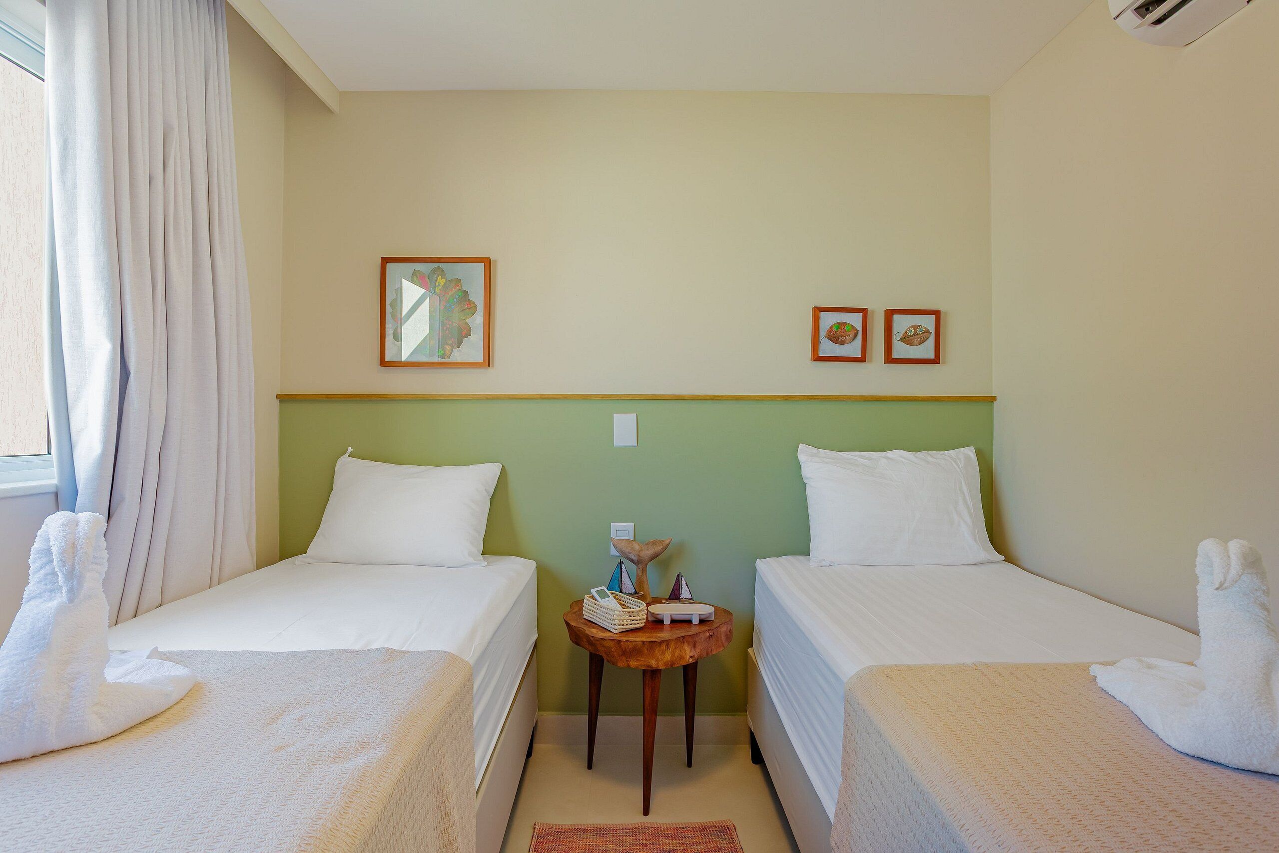 Une chambre d’hôtel avec deux lits simples, une petite table agrémentée d’objets décoratifs et une fenêtre avec des rideaux.