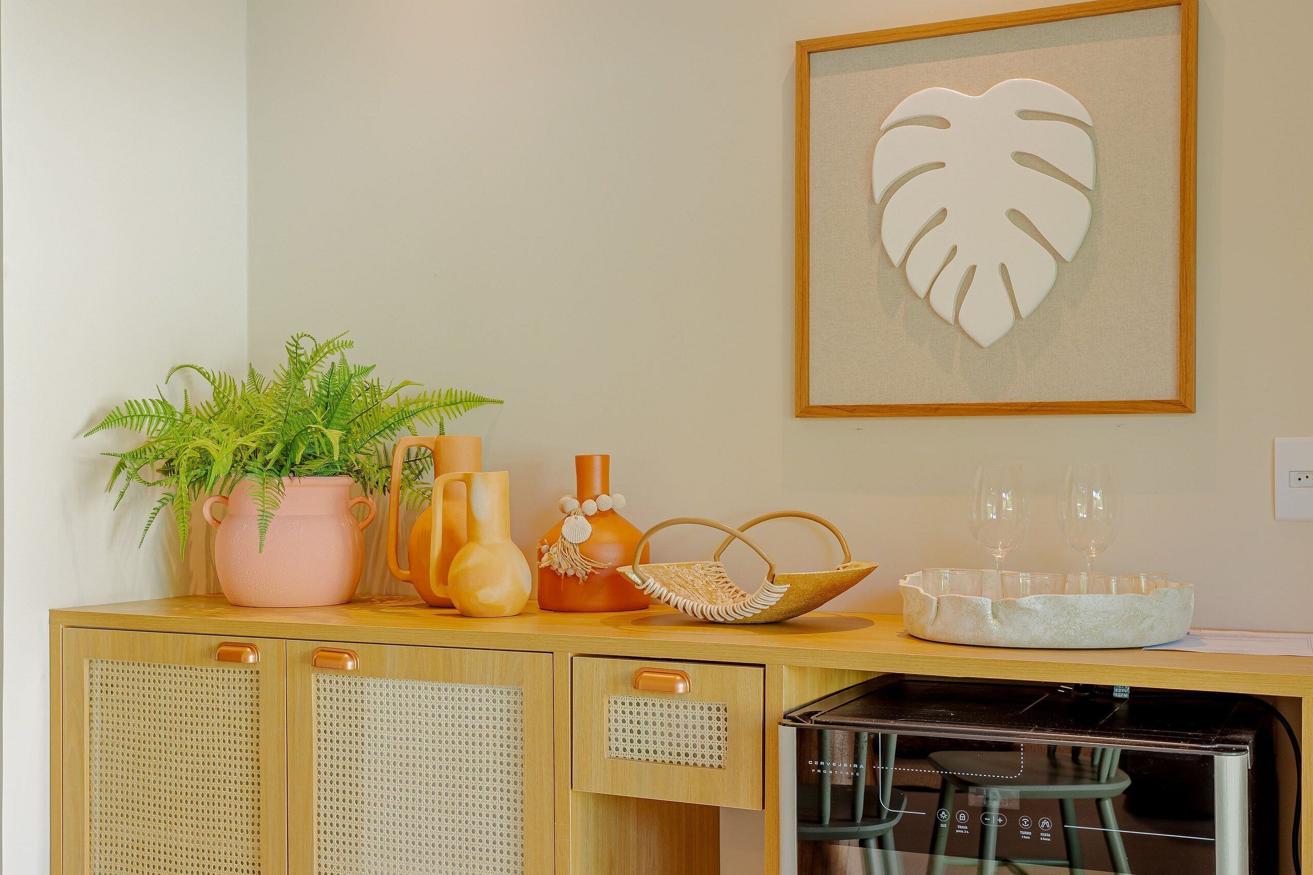 Una encimera de cocina con una planta en maceta, jarrones decorativos, una cesta tejida y una obra de arte enmarcada.