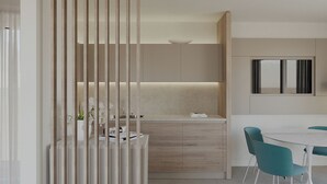 A modern kitchen with a central island, a dining area with teal chairs, and a large window.