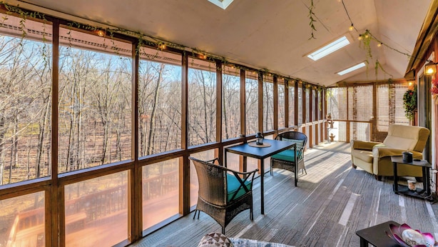 Una habitación amplia con ventanas grandes, suelo de madera, una mesa con sillas y un sofá.