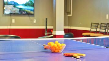 A ping pong table with a net, a bowl of ping pong balls, and a table tennis paddle.