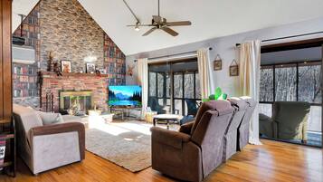 Una sala de estar acogedora con chimenea, televisor y un amplio ventanal con vistas a un paisaje nevado.