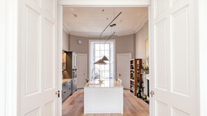 A spacious kitchen with a central island, white cabinetry, and a large window providing natural light. - Stunning 4 bedroom Townhouse in central Edinburgh with garden & private parking (Edinburgh)