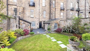 A stone building with multiple windows and balconies, a small garden with stepping stones, and a paved entrance. - Stunning 4 bedroom Townhouse in central Edinburgh with garden & private parking (Edinburgh)