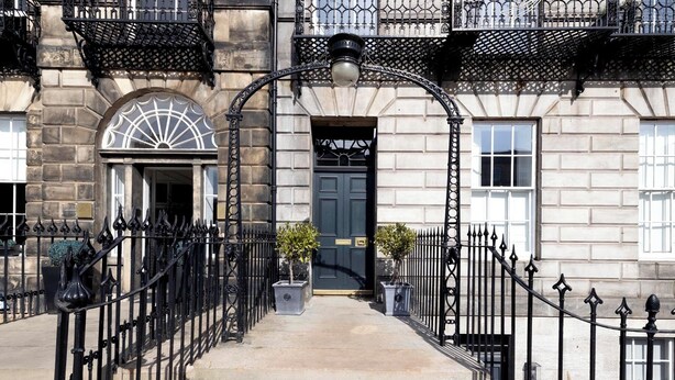 A traditional stone building with a black iron gate, a central door, and a small garden area with potted plants. - Stunning 4 bedroom Townhouse in central Edinburgh with garden & private parking (Edinburgh)