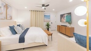 Un dormitorio moderno con cama, televisor, ventilador de techo y mesita de noche.