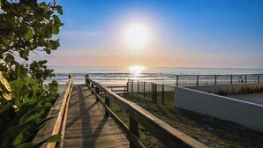 Una pasarela de madera que conduce a una playa, con una valla y vista despejada al océano.